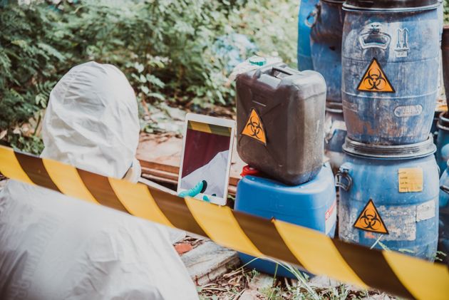 A person in a protective suit is standing next to a stack of barrels.