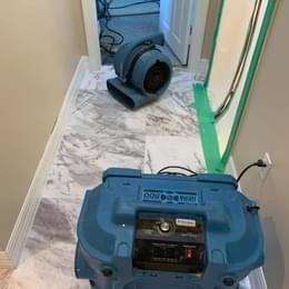 A blue dryer is sitting on a tiled floor in a hallway.