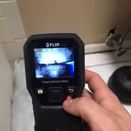 A person is holding a flir moisture meter in their hand.
