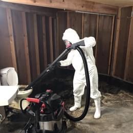A person in a protective suit is using a vacuum cleaner in a bathroom.