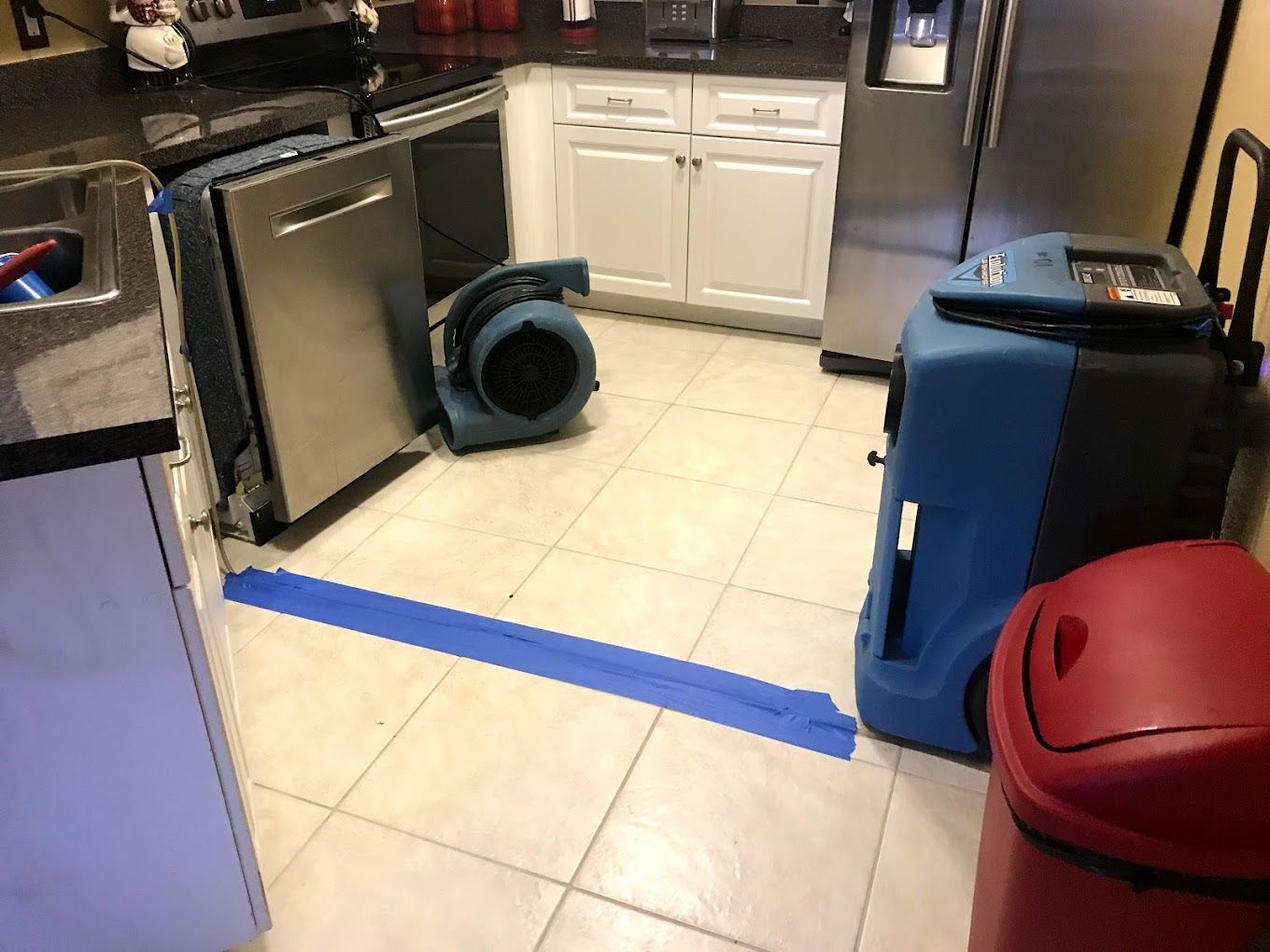 Kitchen with water damage restoration equipment, including fans and a dehumidifier, on a tiled floor.