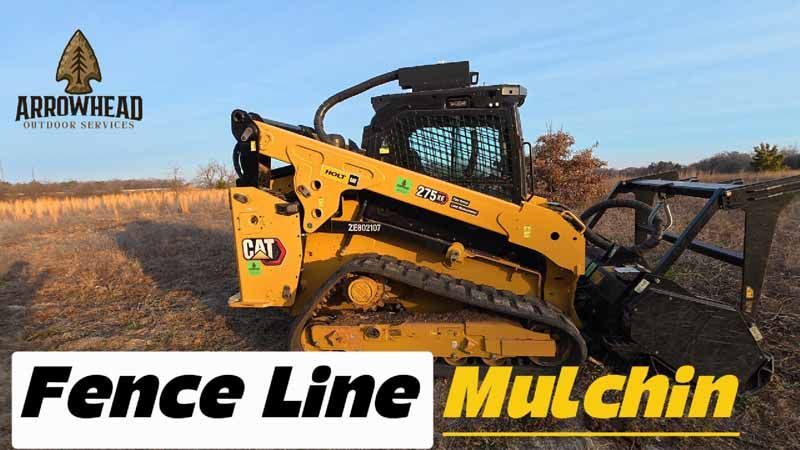 A yellow Caterpillar compact track loader with a mulcher attachment sitting in a field under a clear blue sky.