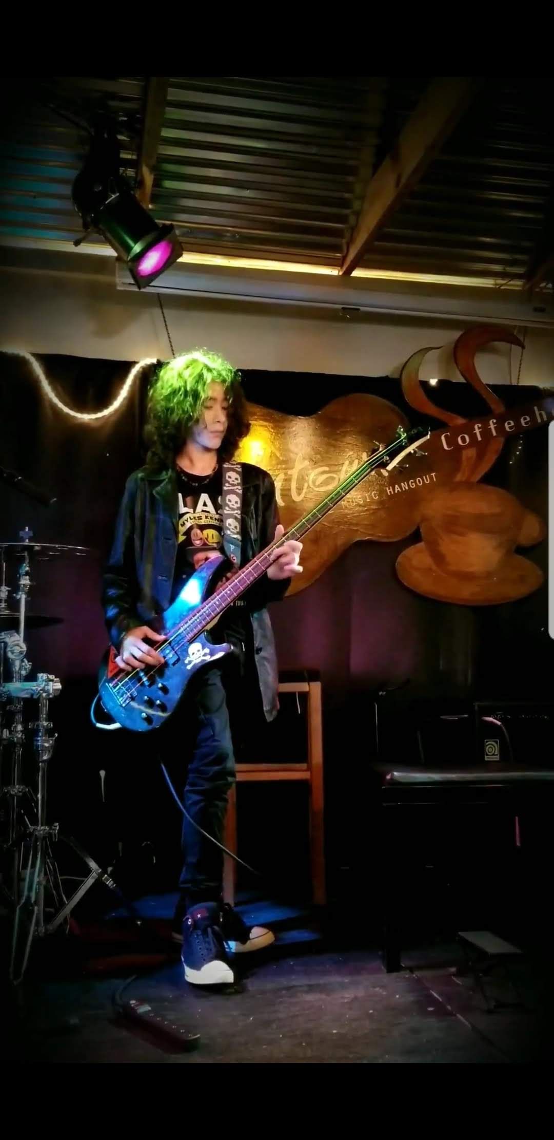 Milo in a coffee shop playing bass in a leather jacket