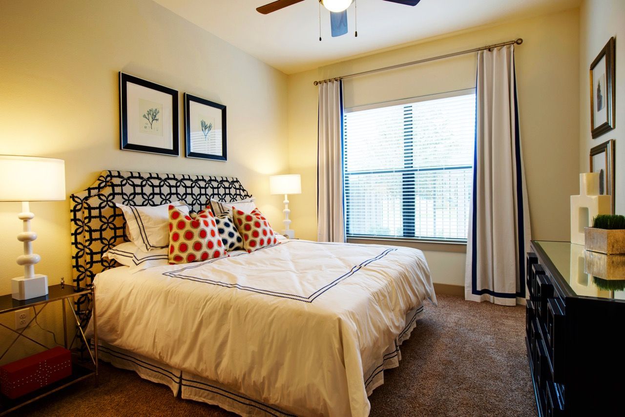 Bedroom in an apartment with a large bed, two nightstands, lamps, window, and dresser.