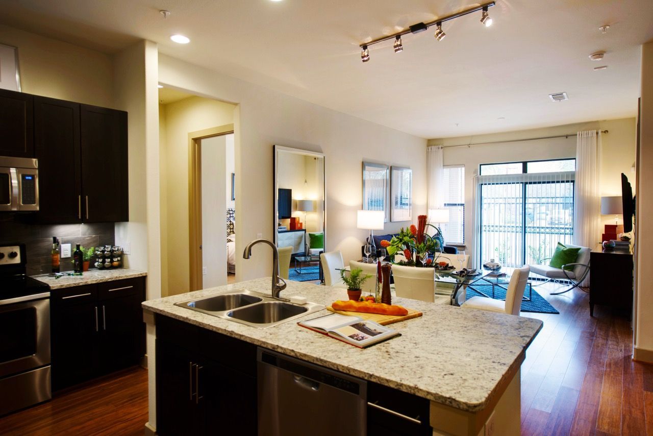 Open-concept apartment kitchen and living area with island, stainless appliances, and bright seating area.