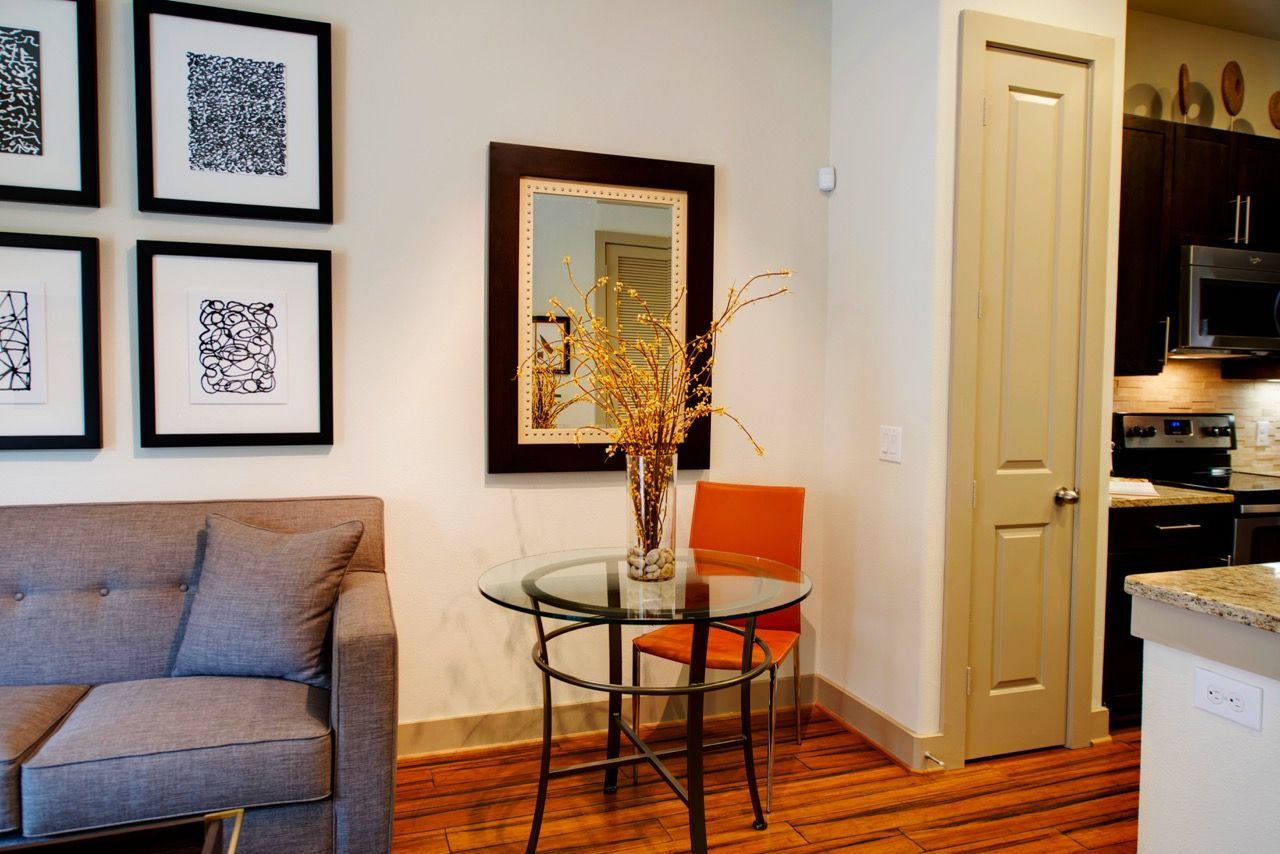 Living room in an apartment with a round glass table, orange chair, and framed wall art.