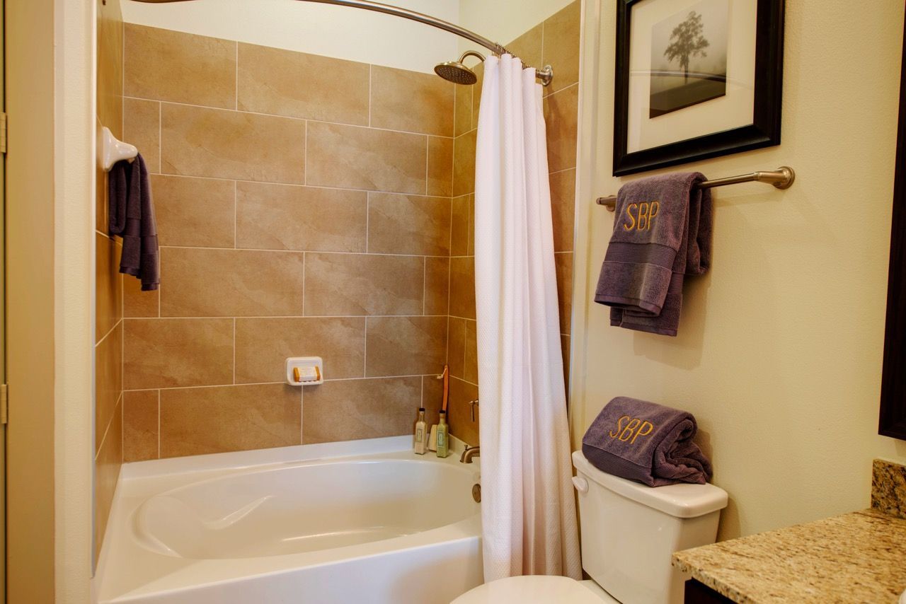Bathroom in apartment with a tiled shower/tub, white curtain, towel rack, and granite countertop.
