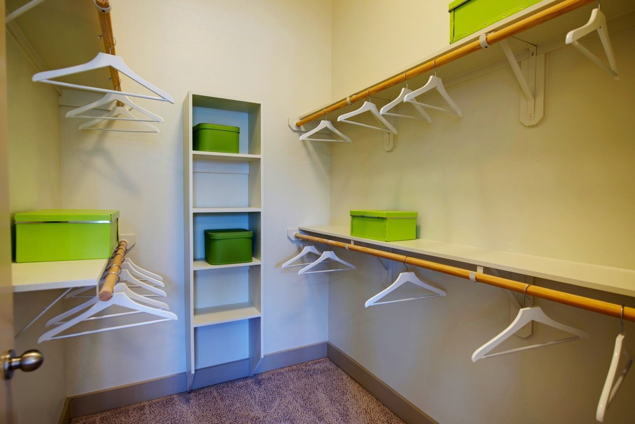 Walk-in closet with white hangers, shelves, and lime green storage boxes.