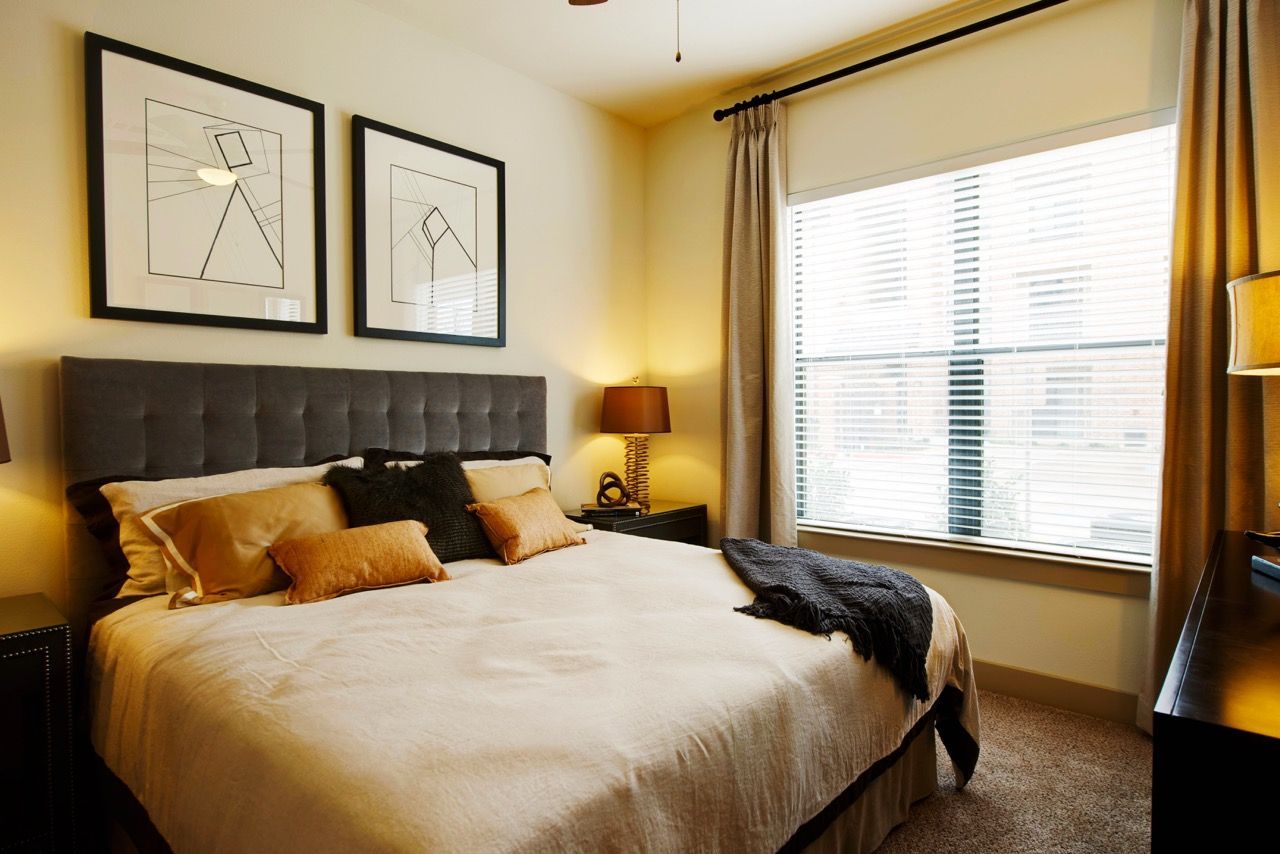 Bedroom with upholstered headboard bed, two nightstands, lamps, and a large window with blinds.