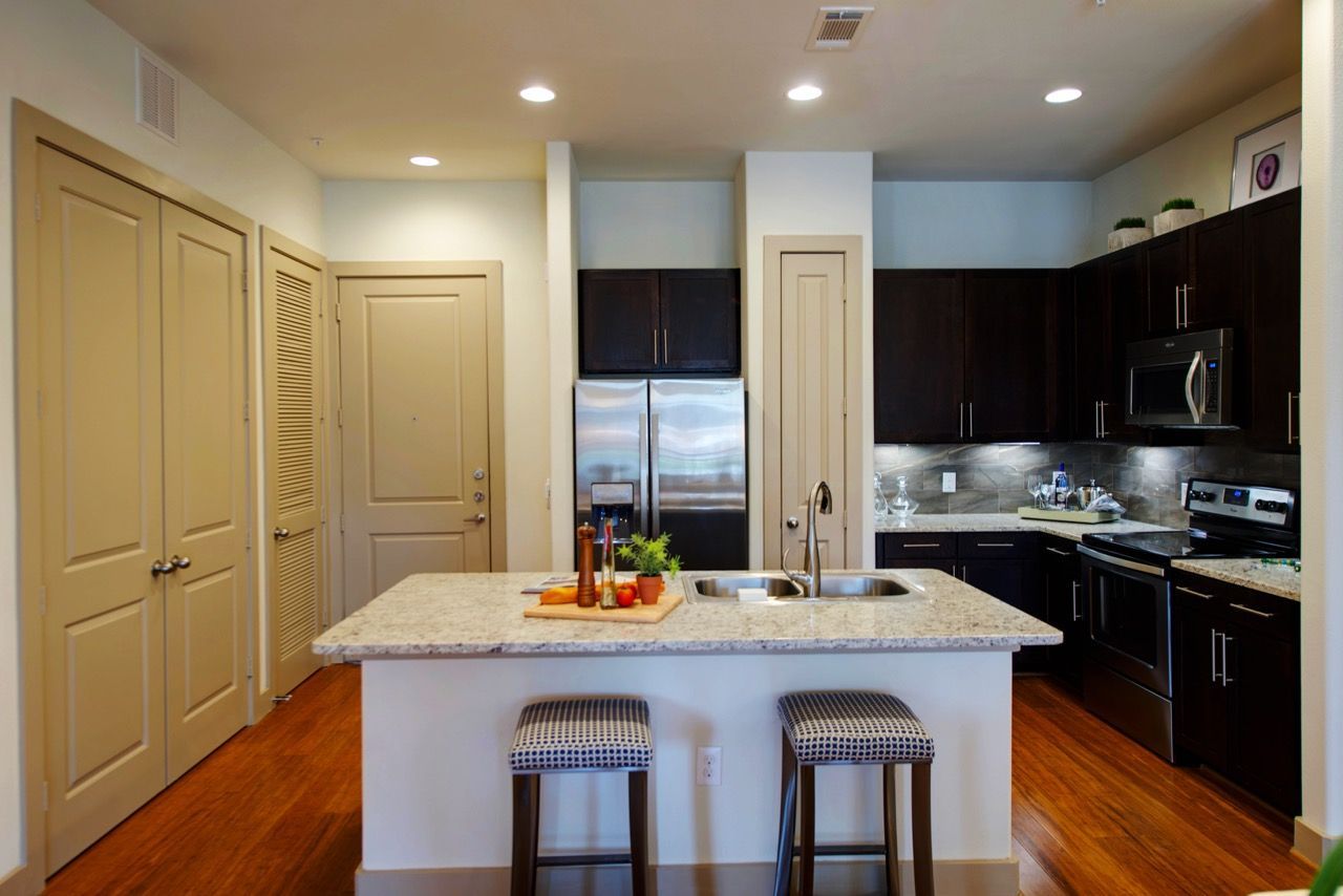 Modern kitchen with an island, granite countertop, dark cabinets, and stainless steel appliances.