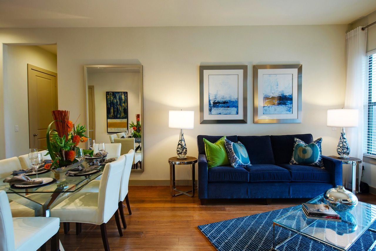 Living room and dining area in a modern apartment with a blue sofa and glass coffee table.