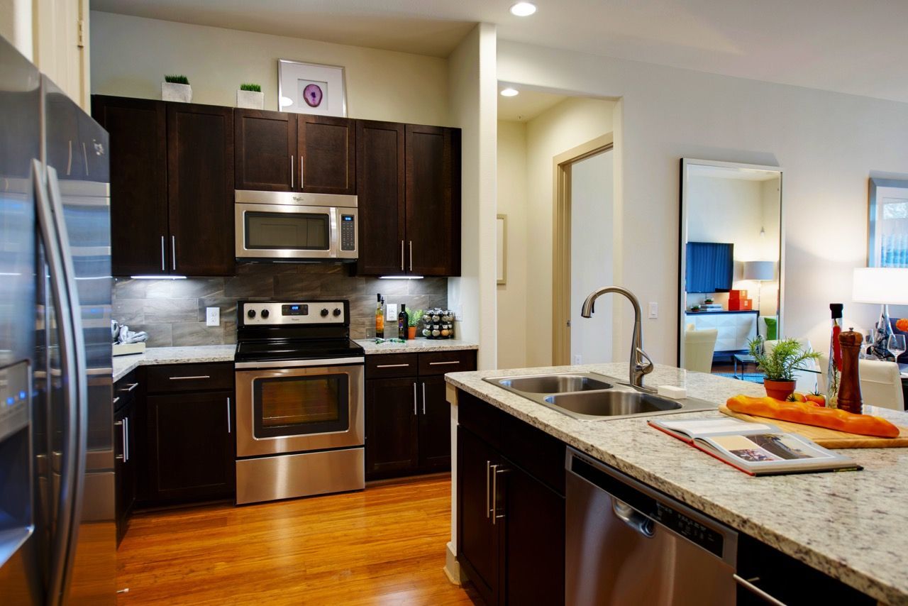 Modern apartment kitchen with dark wood cabinets, stainless steel appliances, and an island sink.