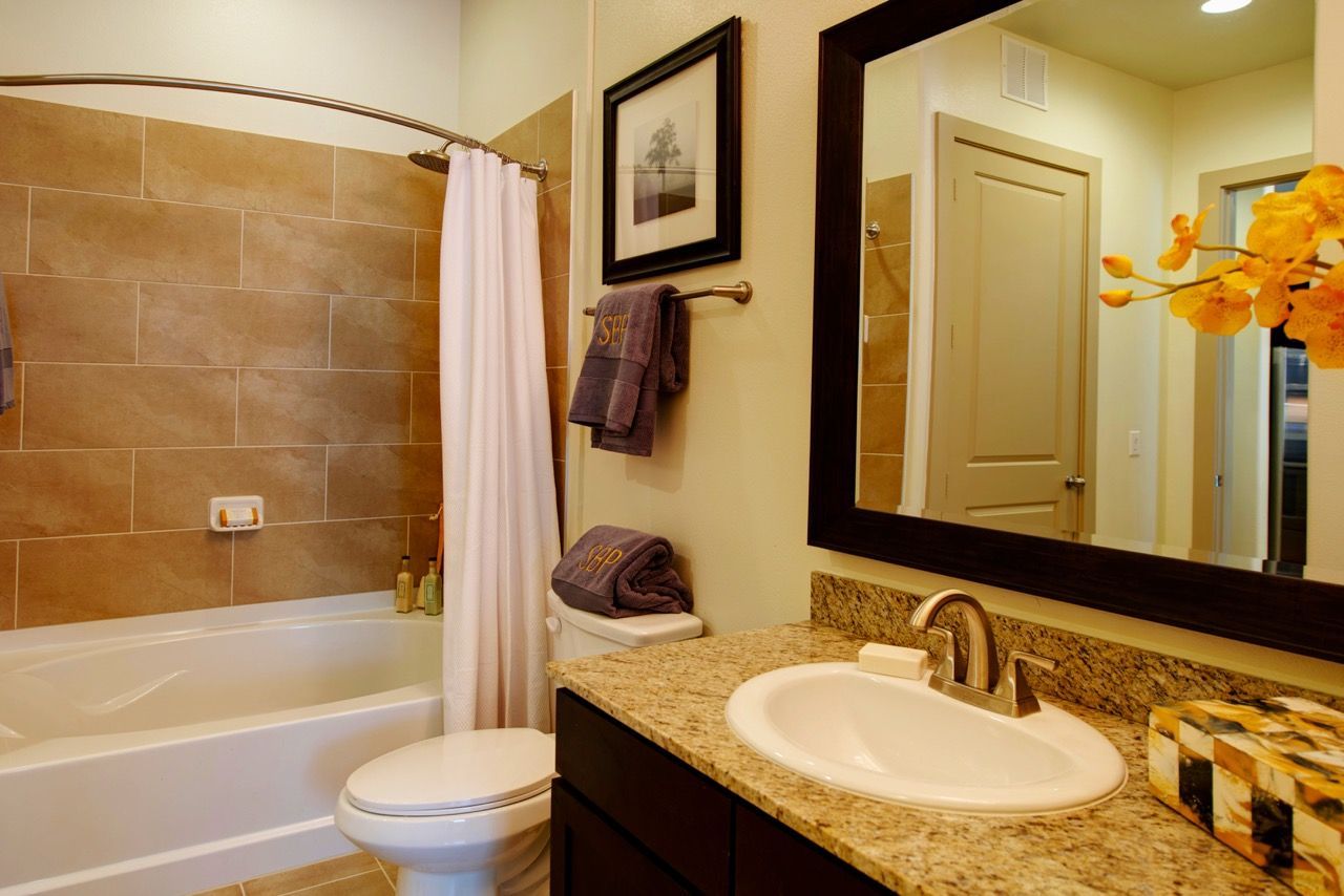 Bathroom interior with a bathtub and shower curtain, toilet, and granite countertop sink.