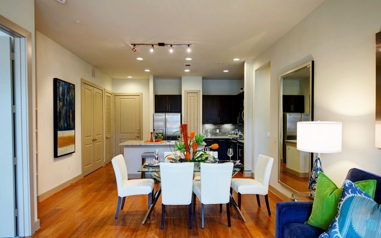 Open-concept dining area with a glass table and white chairs near a modern kitchen.