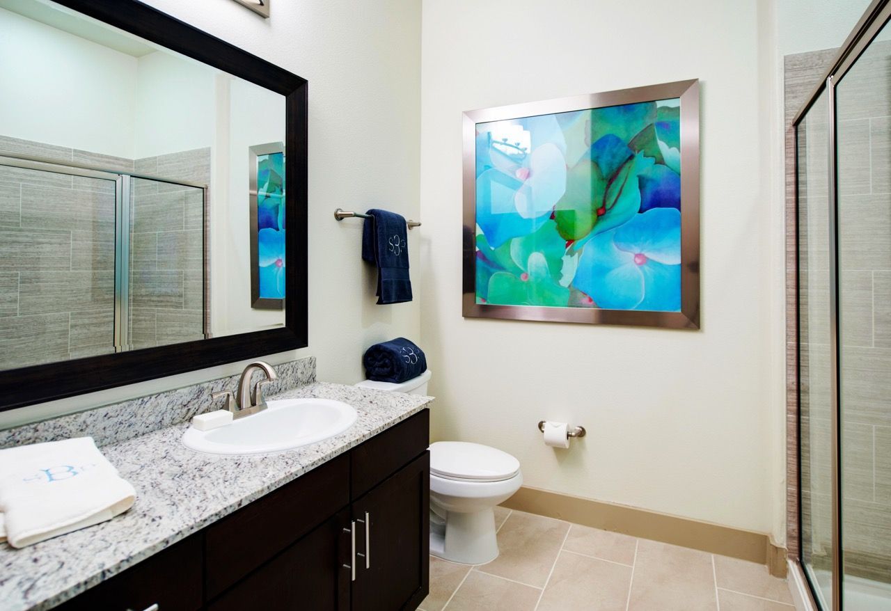 Bathroom featuring a granite countertop, single sink, large framed mirror, towels, and a glass shower.