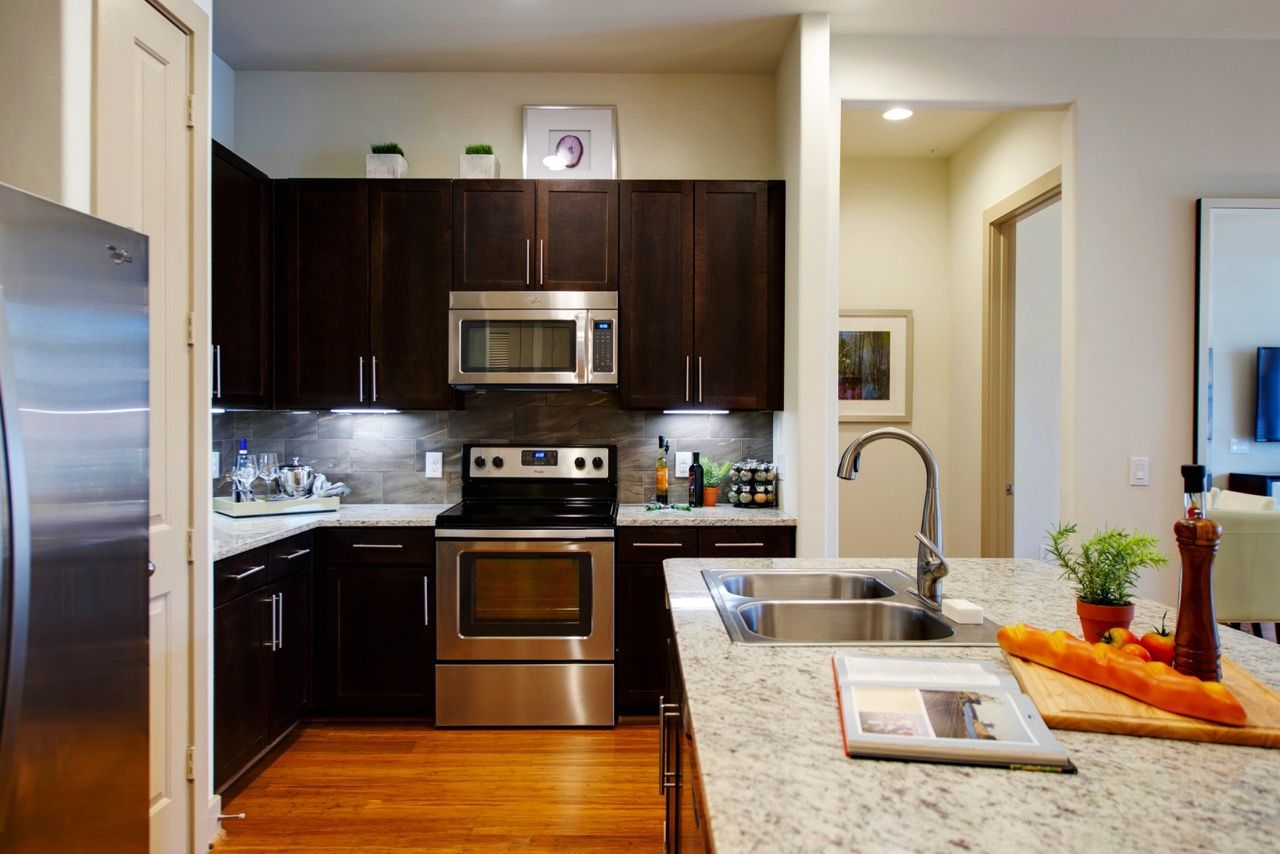 Modern kitchen with dark wood cabinets, stainless steel appliances, and an island sink.