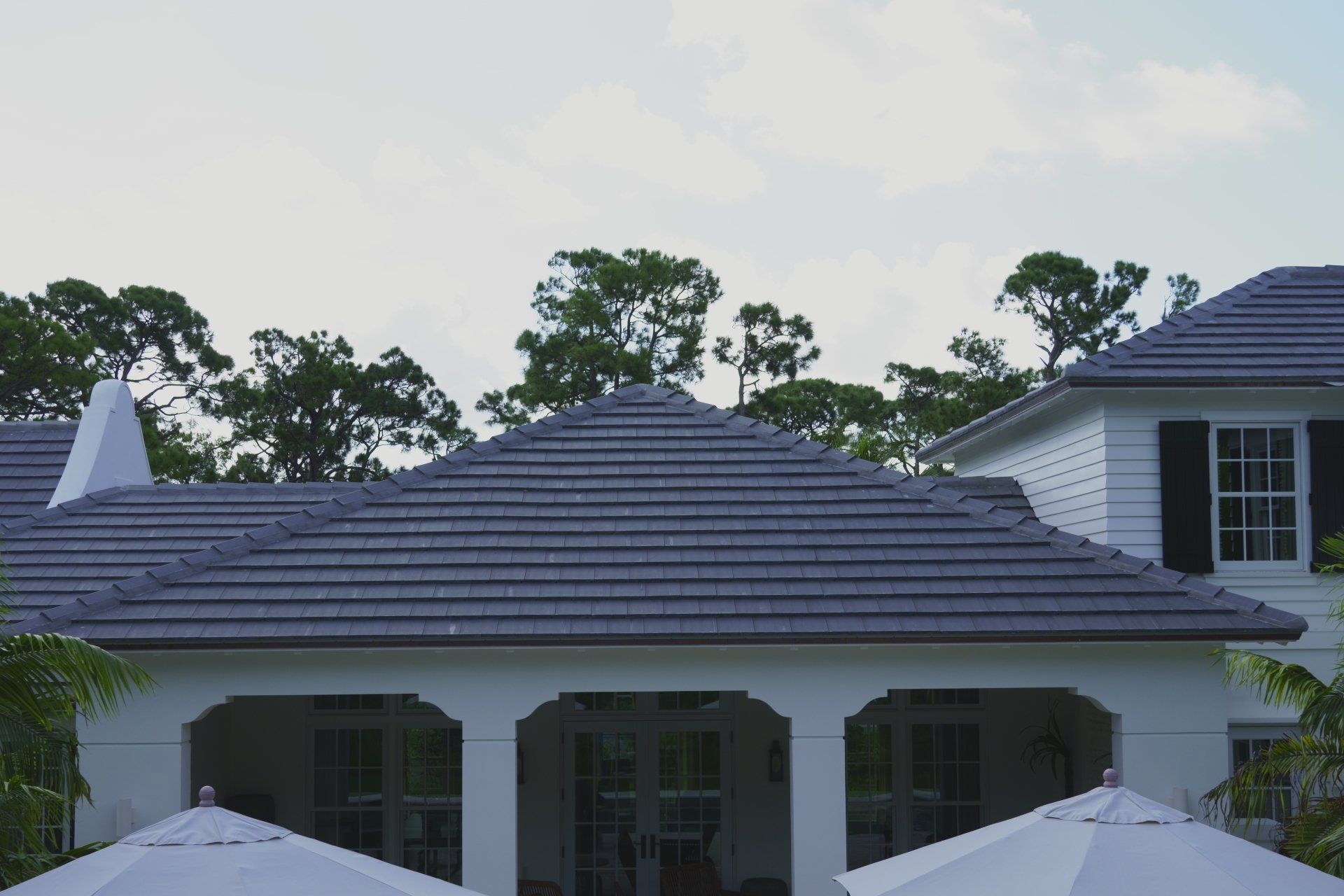 White house with dark gray tiled roof, arched porch, trees and cloudy sky.