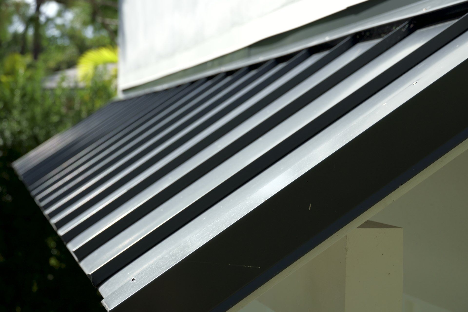 Dark metal roof with parallel ridges, angled away from a white building.