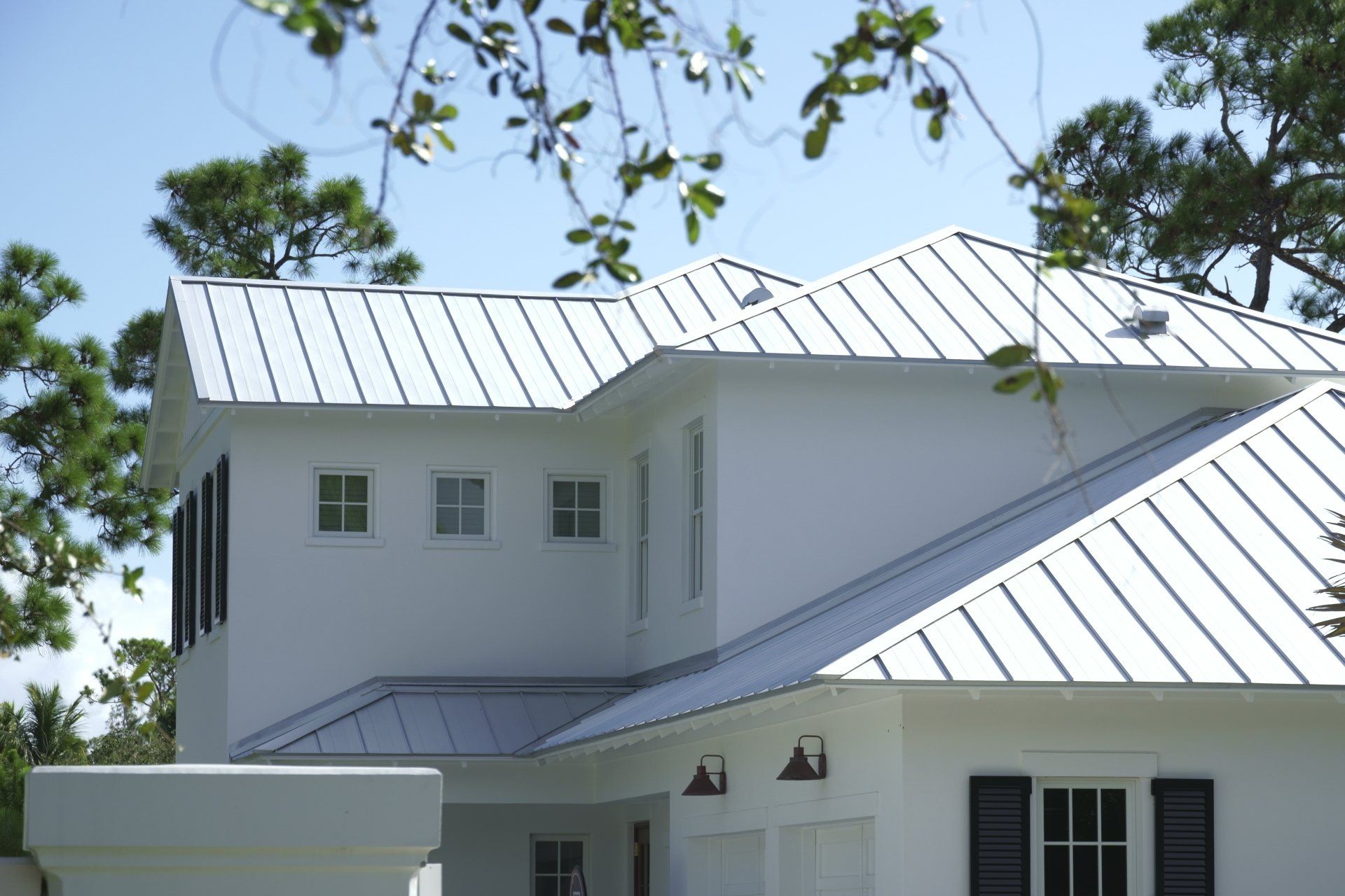 White house with silver metal roof, black shutters, and clear blue sky.