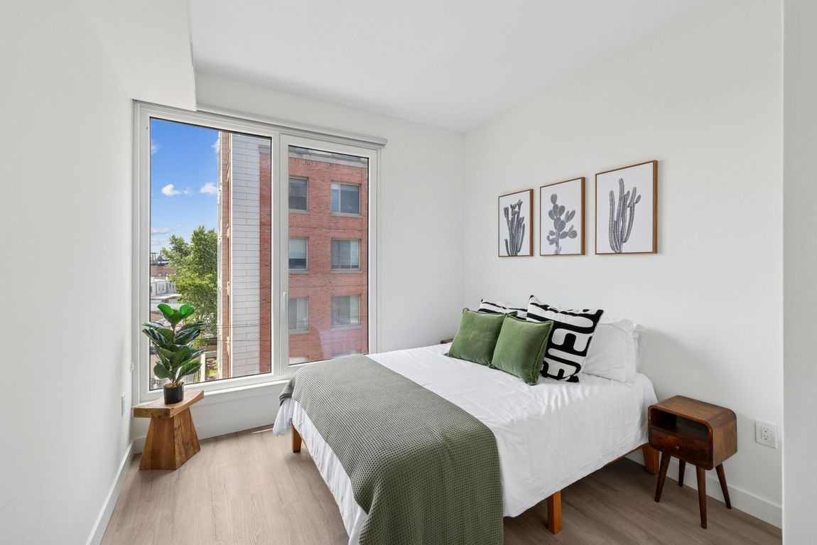 A bedroom with a bed and a window with a brick building in the background.