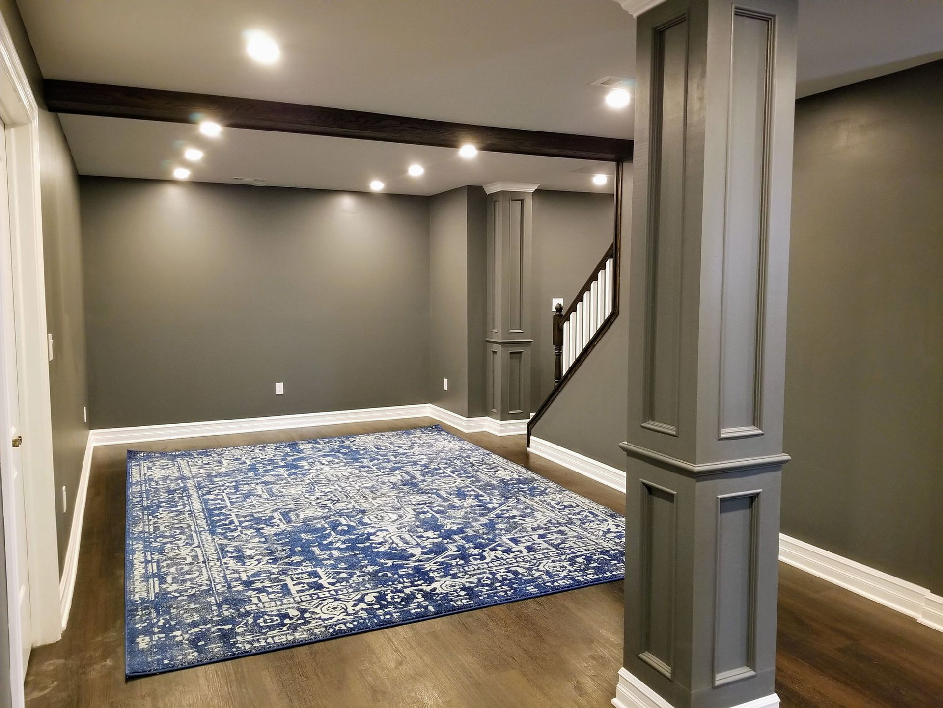 An empty basement with a blue rug and a staircase.