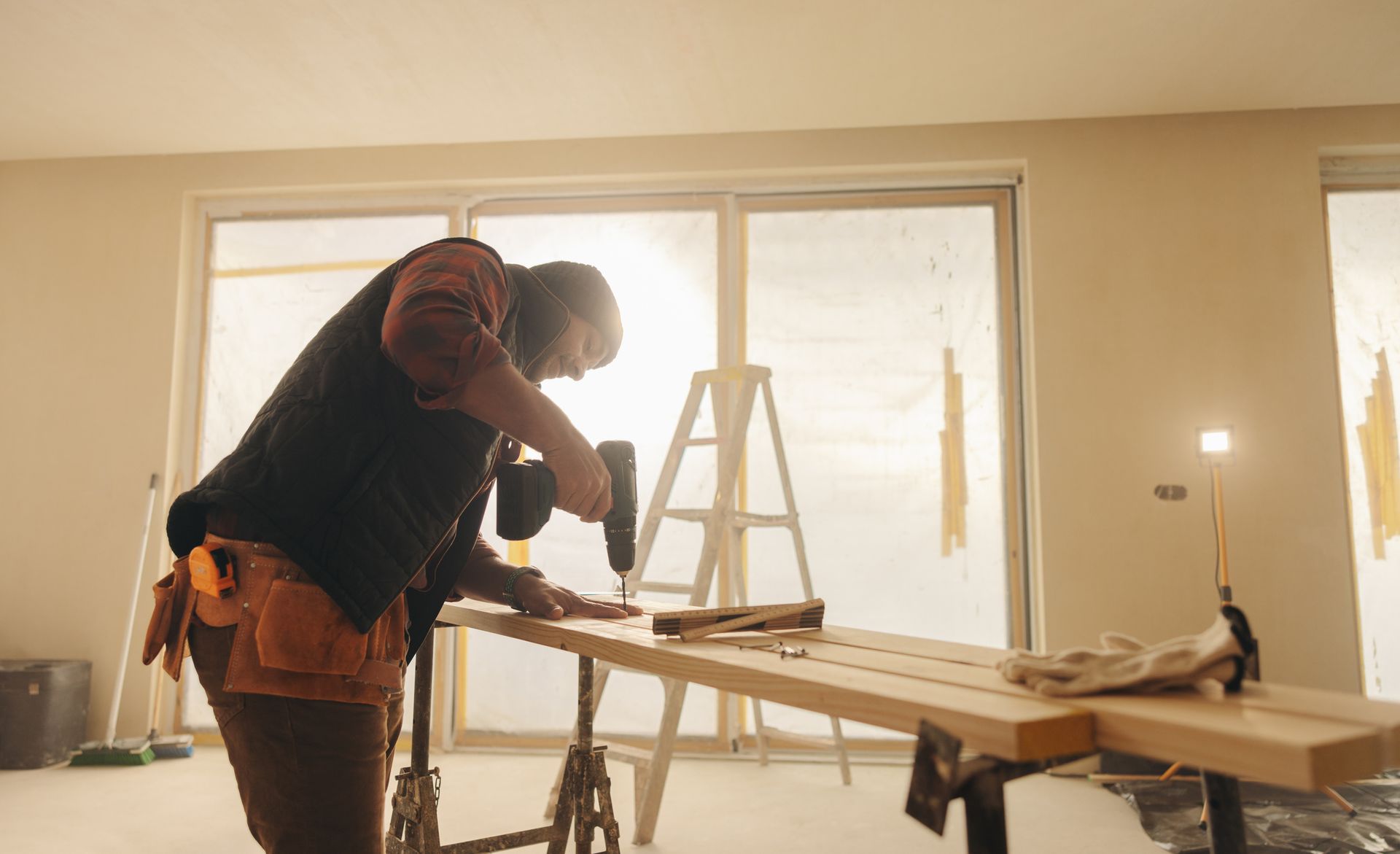 Construction worker using power drill on wooden boards during home renovation project.