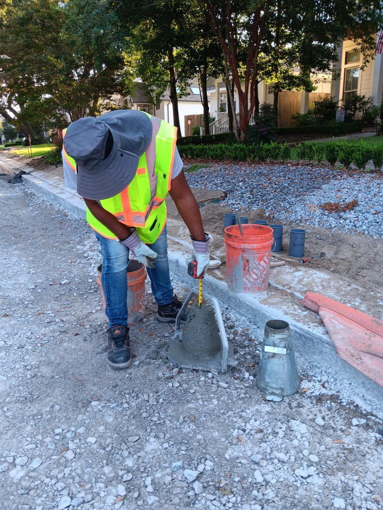 A person in a high-visibility vest and sun hat performs a concrete slump test on a gravel construction site.