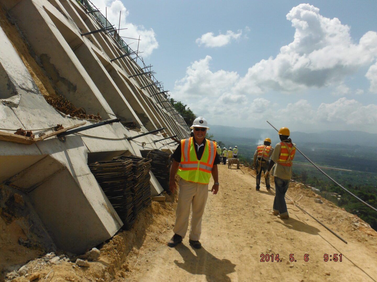People in high-visibility vests work at a construction site beside a concrete retaining wall with anchor cables.
