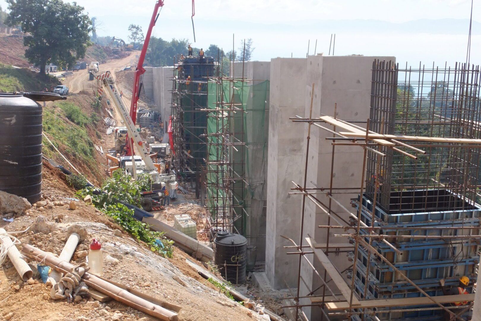 A construction site featuring tall concrete bridge piers under development, surrounded by scaffolding and heavy machinery.