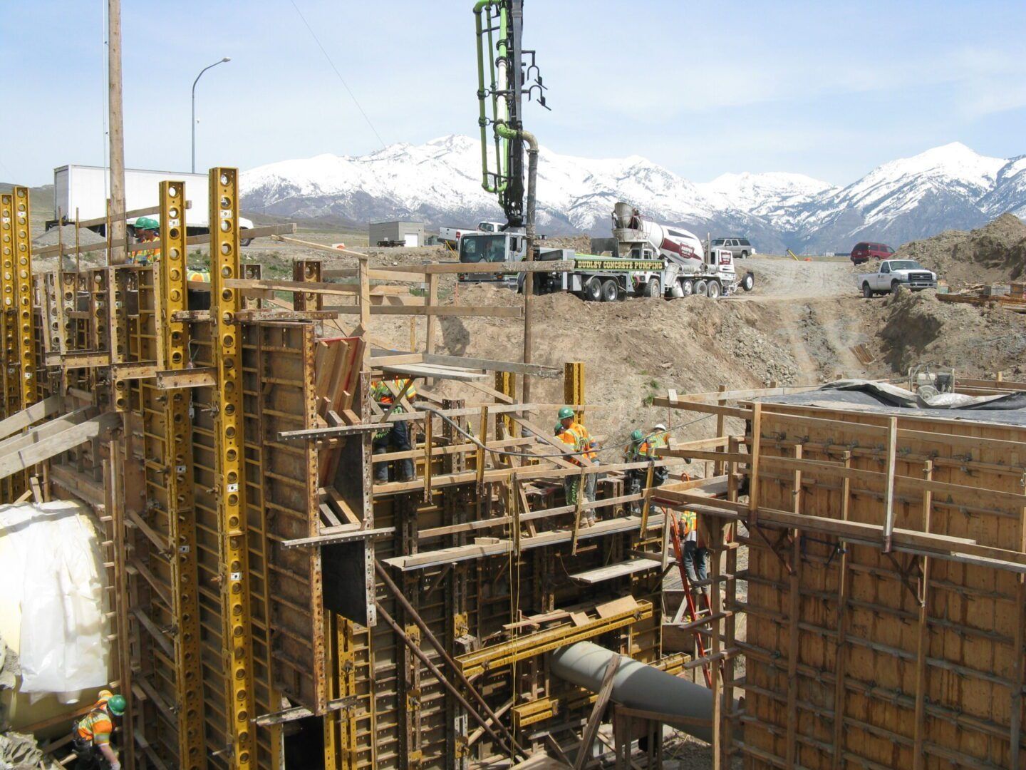 Construction site with scaffolding and wooden forms for concrete pouring, backed by snow-capped mountains.