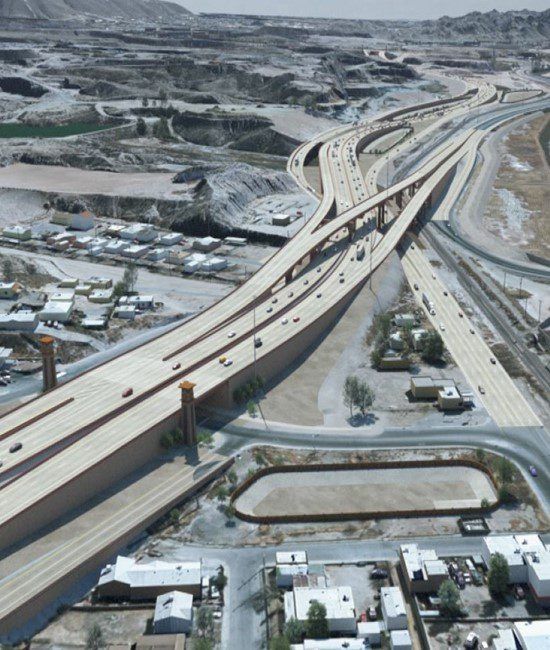 An elevated highway interchange curves through a desert landscape above a neighborhood and an empty, oval-shaped basin.