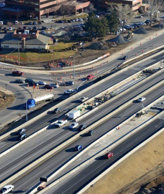 Aerial view of a highway with multiple lanes of traffic, concrete barriers, and an adjacent intersection.