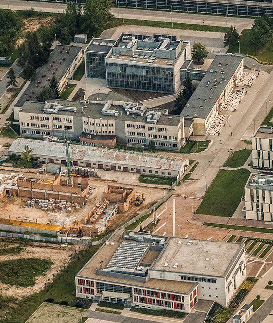 Aerial view of university buildings, a construction site with a crane, and surrounding paths in an urban campus area.