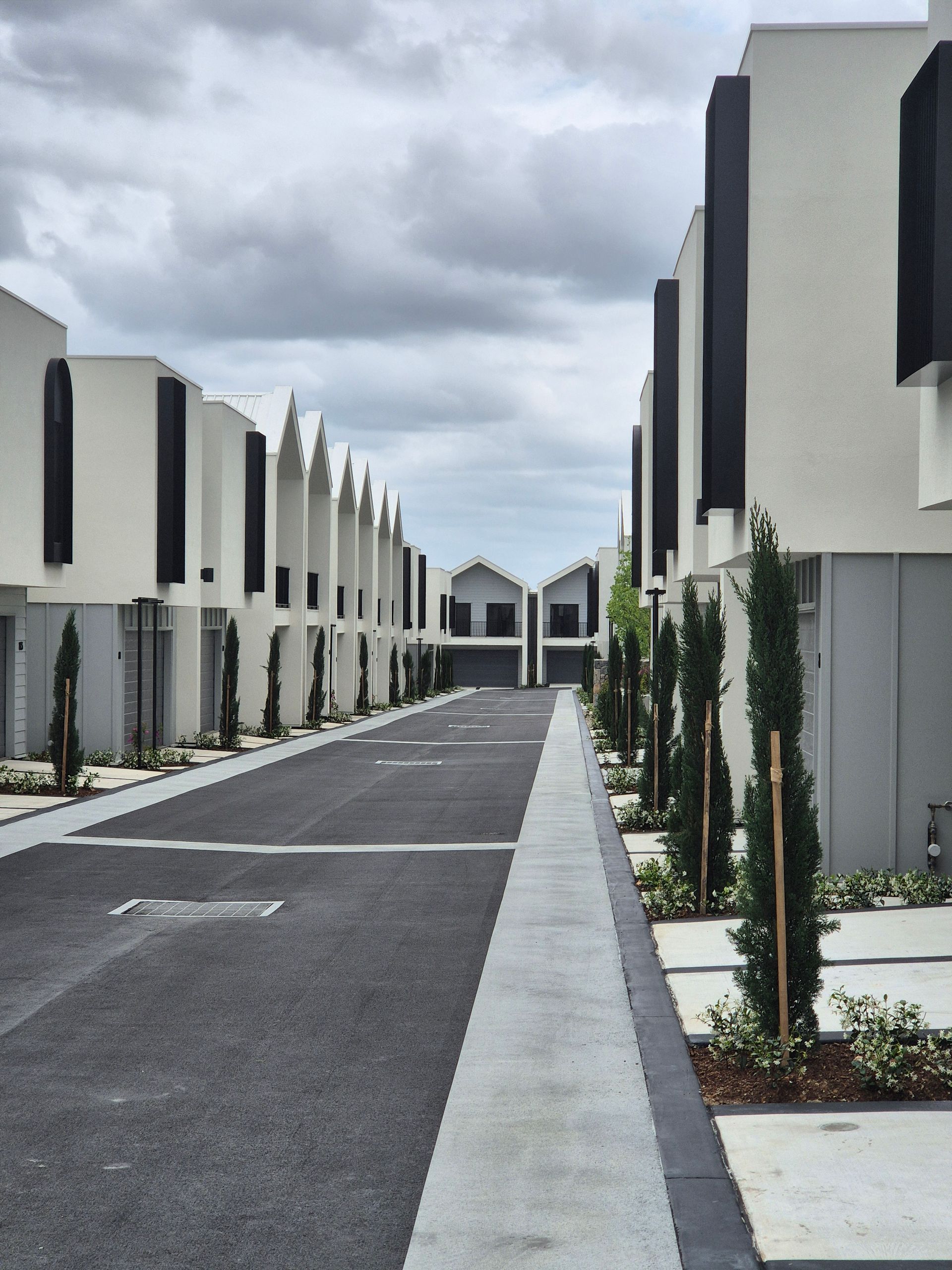 Rows of modern townhouses along a paved road, under cloudy sky.