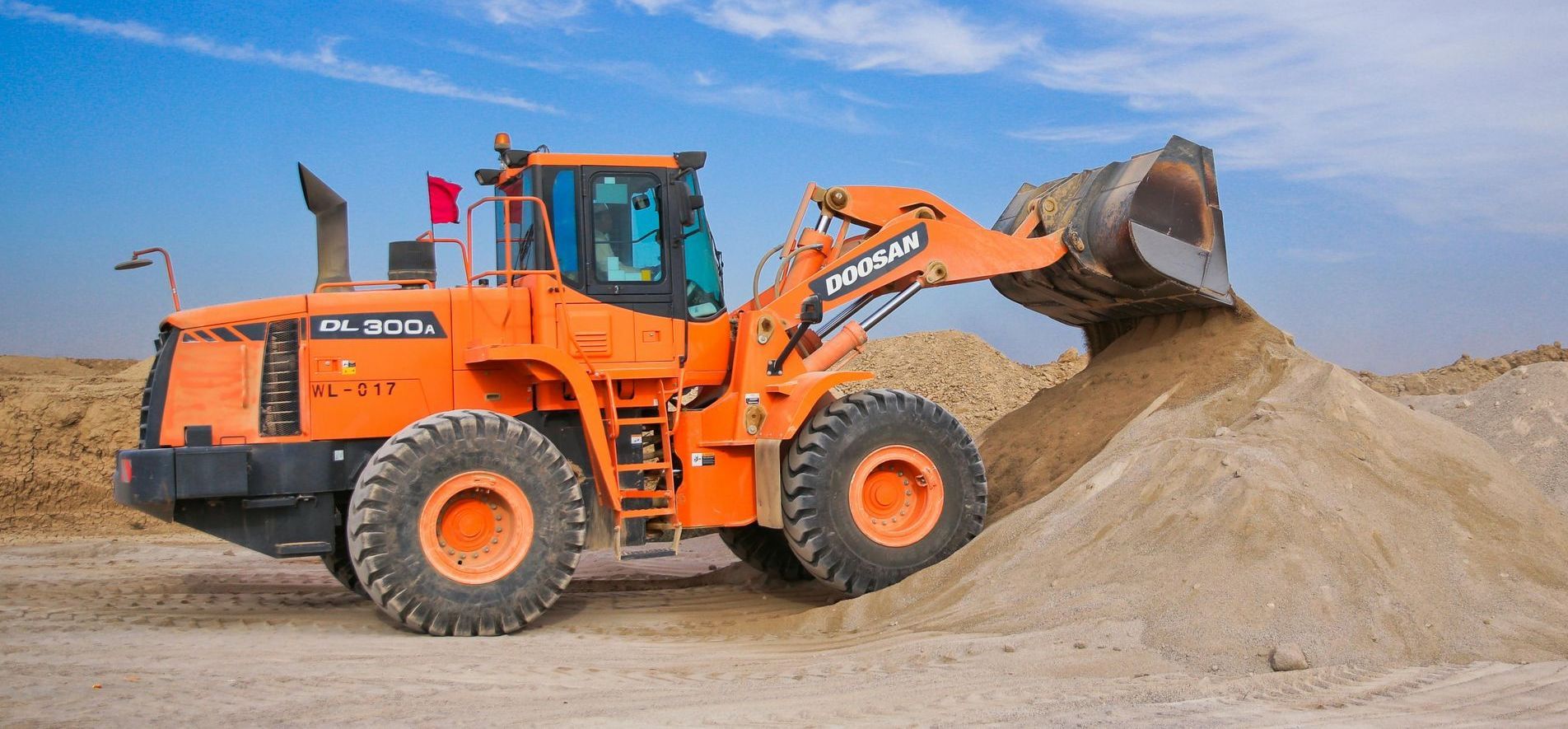 Orange wheel loader dumping sand under a blue sky.