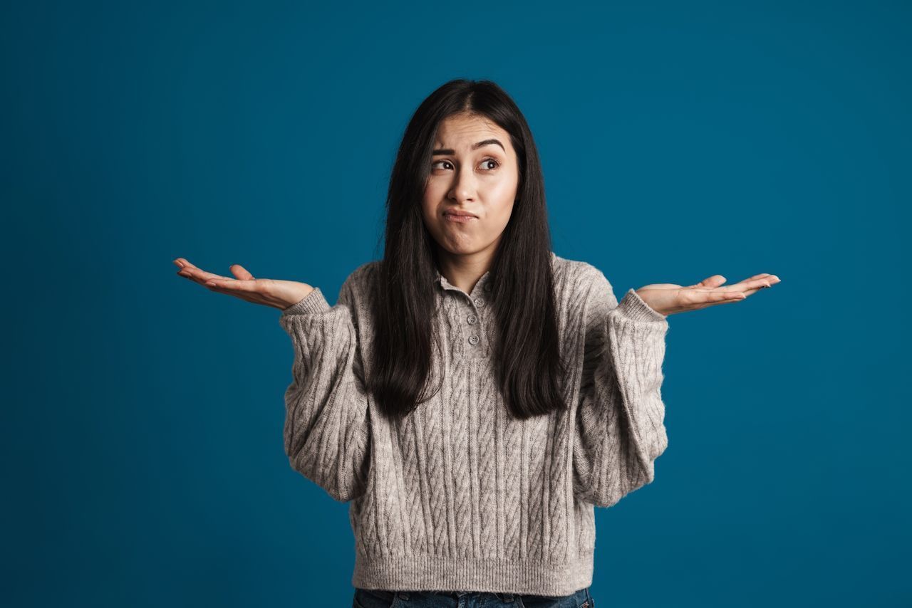 Woman shrugs, palms up, with a puzzled expression against a blue backdrop.