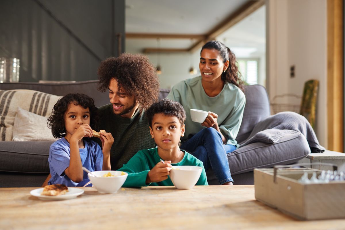 Family enjoying breakfast together in a living room. Smiling parents with two children eating at a coffee table.