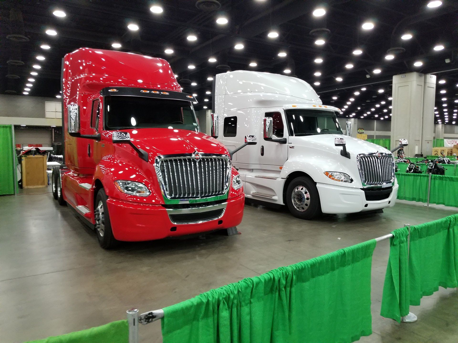 Red and white semi-trucks parked indoors, next to a green barrier.