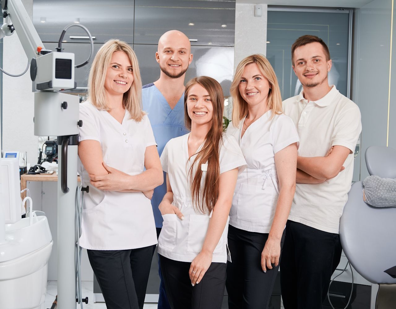 Dental team posing in a modern office, smiling; wearing scrubs and white tops.