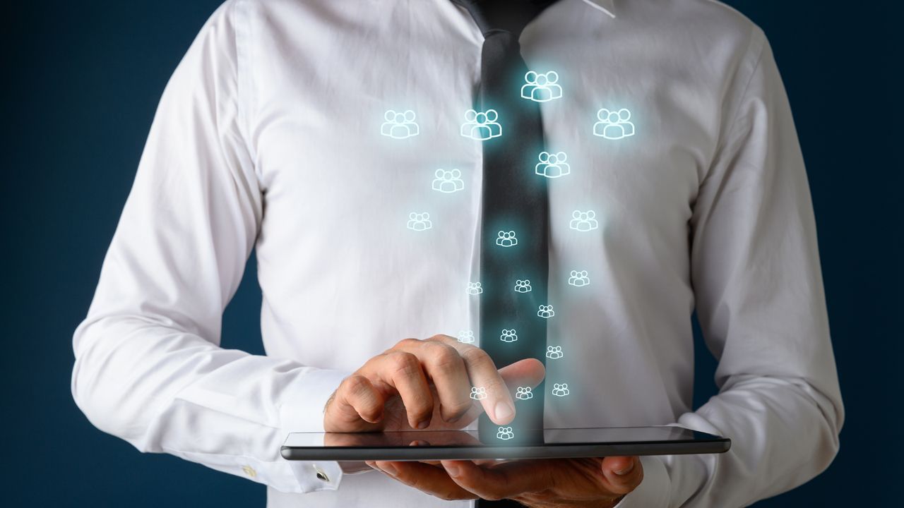 Person in a white shirt and tie using a tablet, with glowing people icons above.