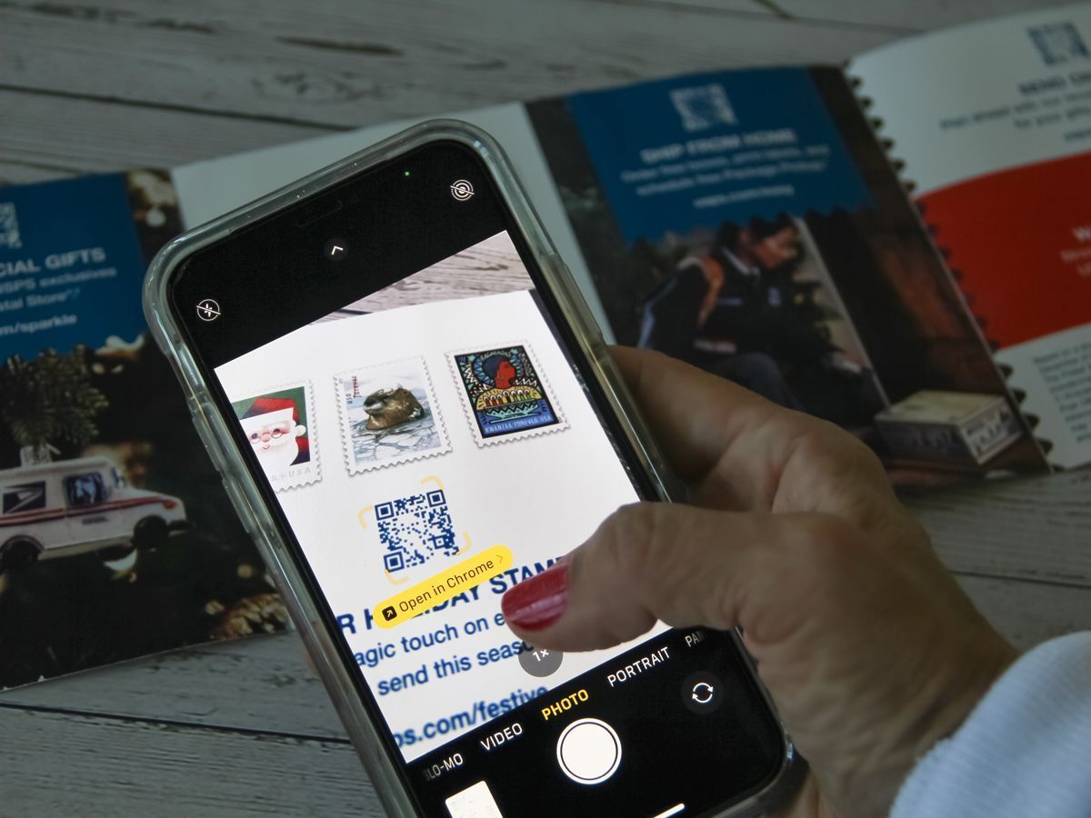 A hand holding a phone scans a QR code over stamps in a postal catalog.