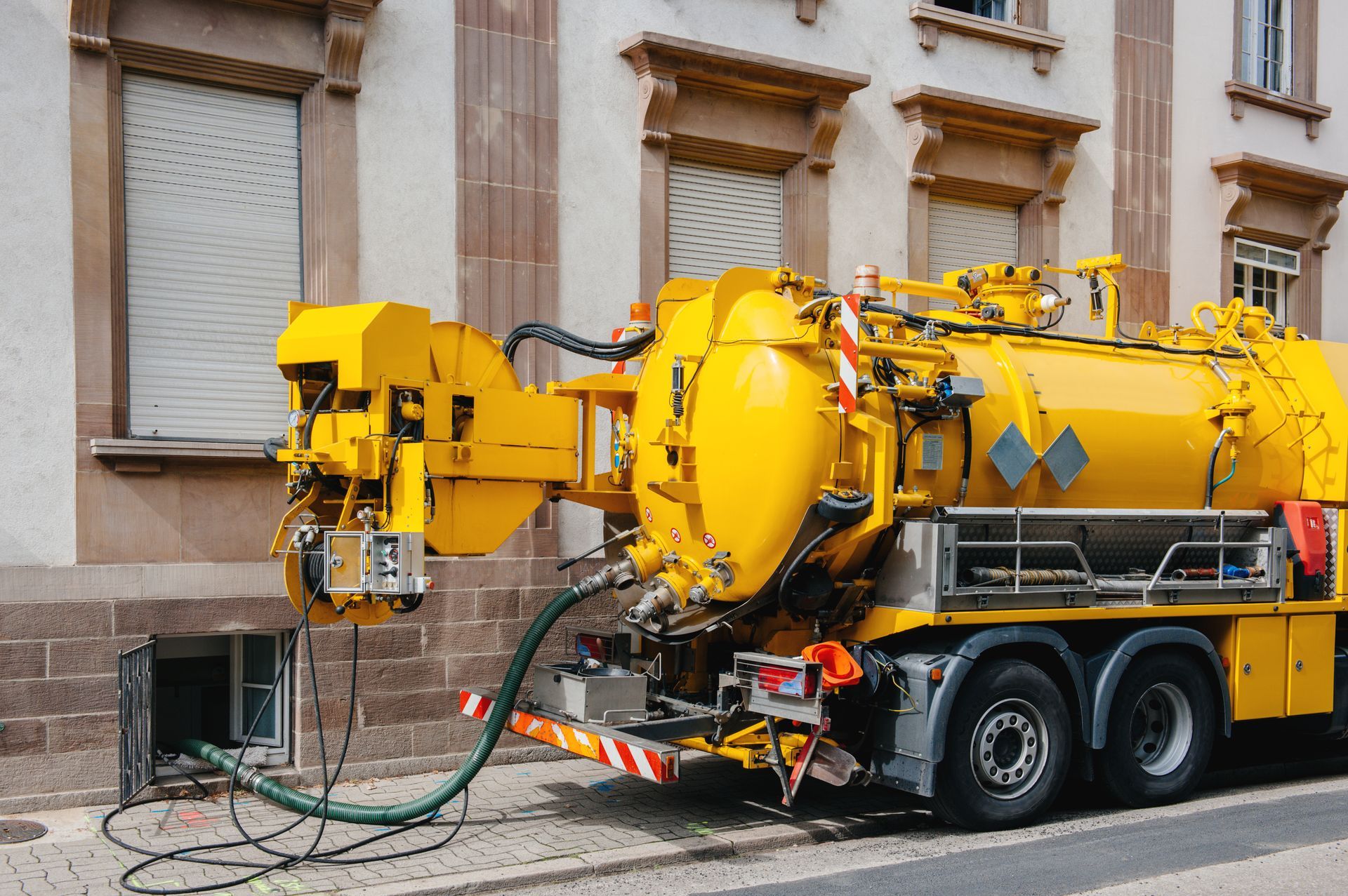 Yellow industrial vacuum tanker truck connected to underground pipe outside a building. Yellow industrial vacuum tanker truck connected to underground pipe outside a building.