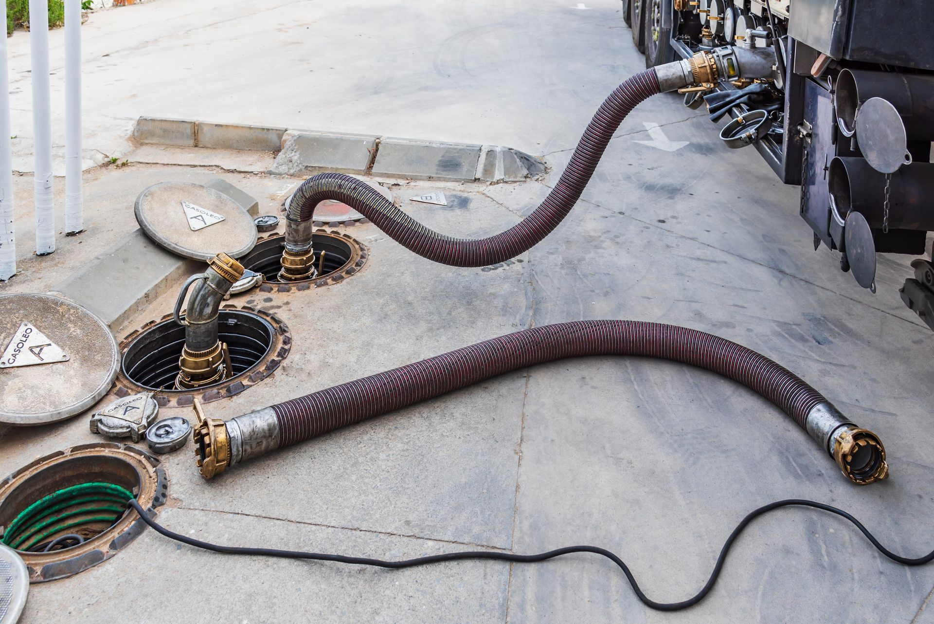 Commercial grease trap cleaning hose inserted into manhole with safety cone nearby.