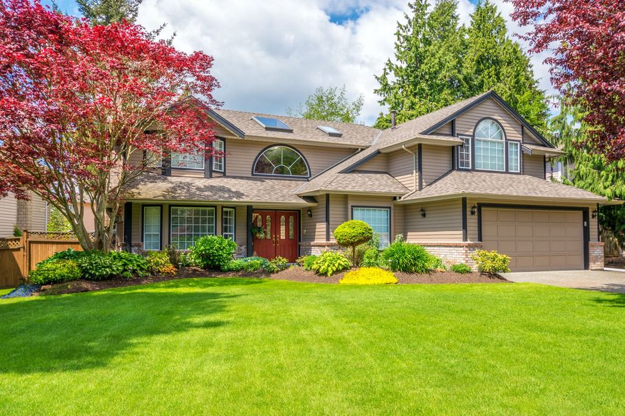 Suburban two-story house with manicured lawn, red-leaf trees, and a bright front facade
