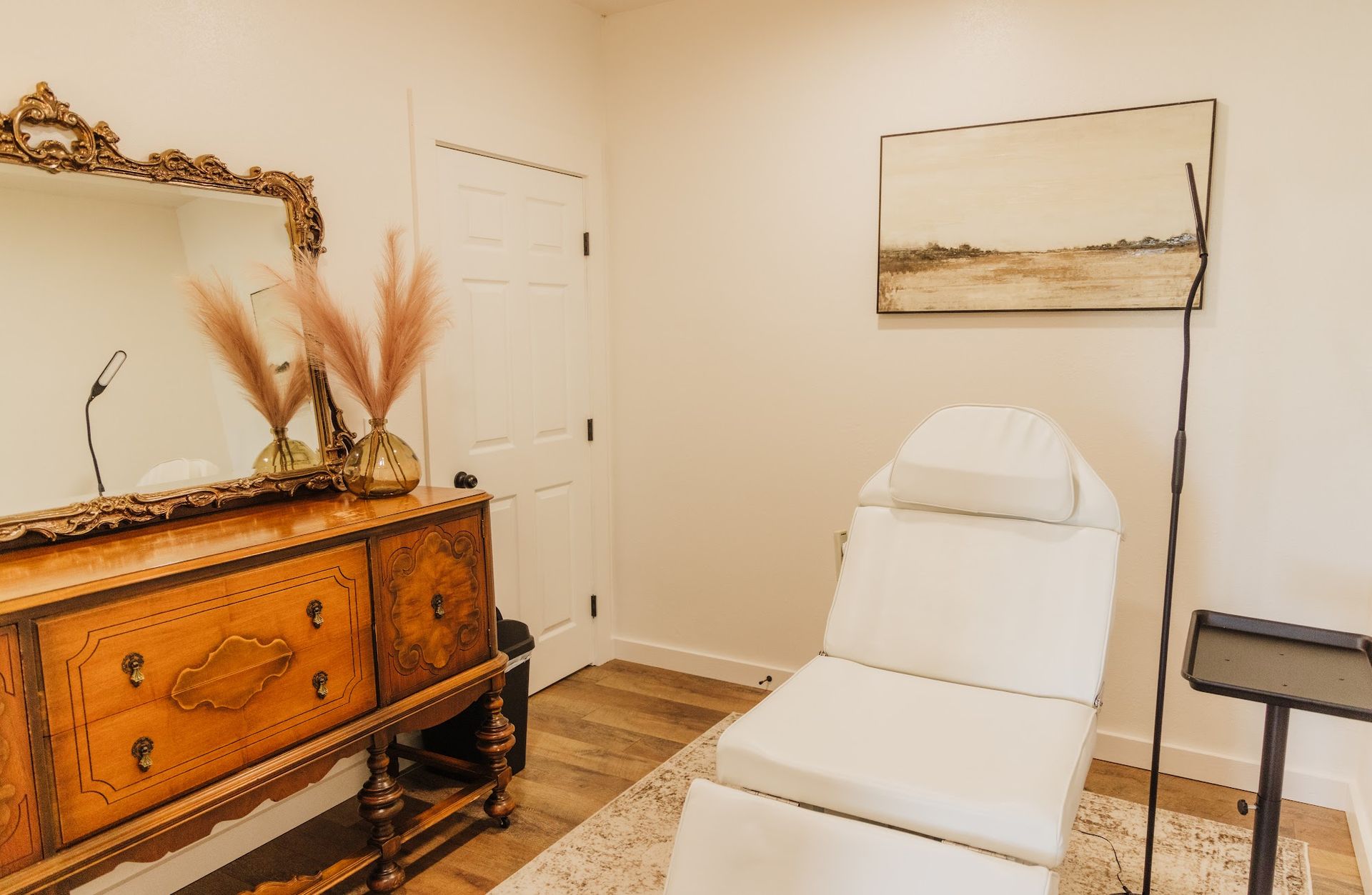 A room with a chair , dresser , mirror and painting on the wall.