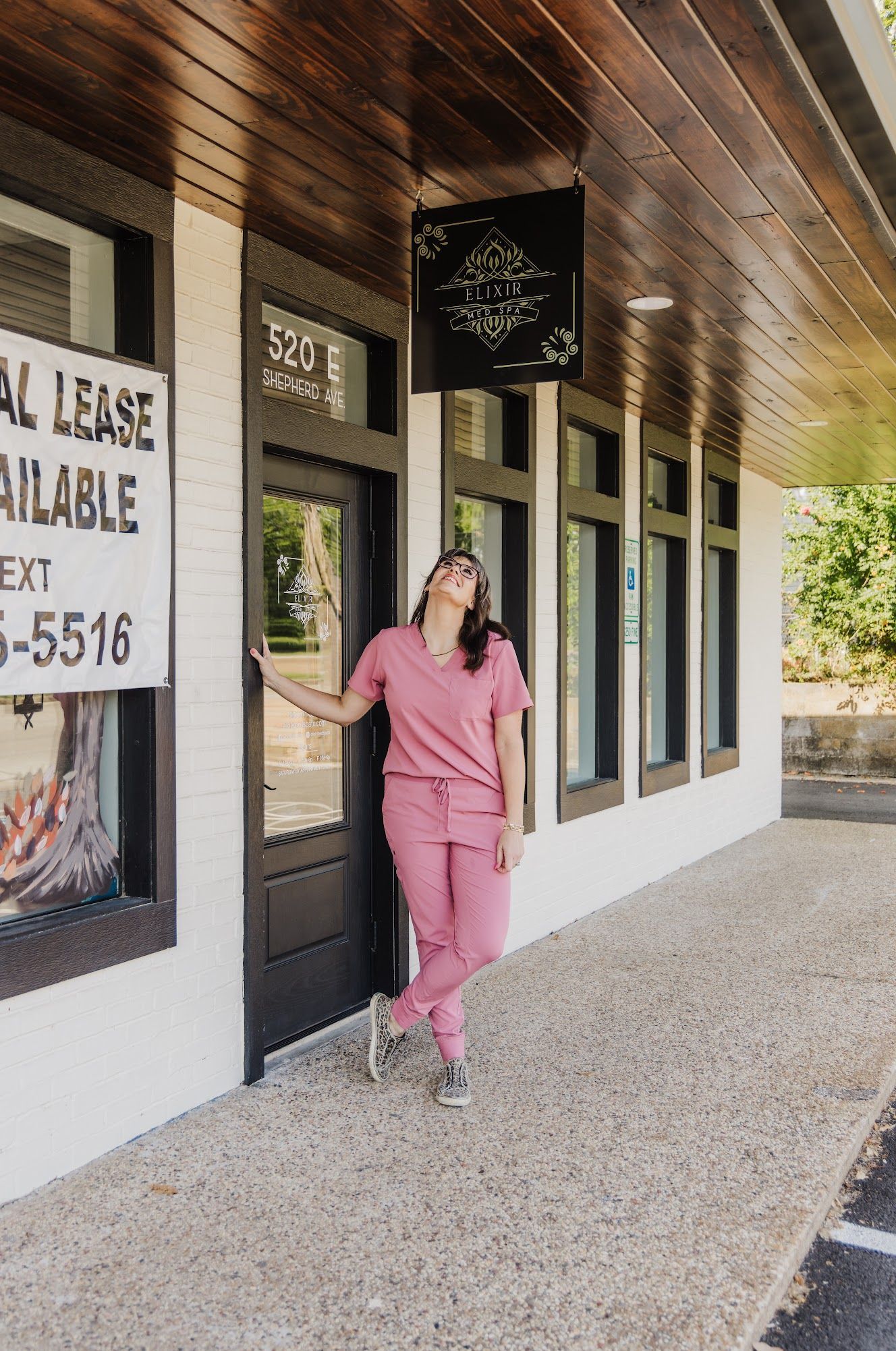 A woman in pink scrubs is standing in front of a building.