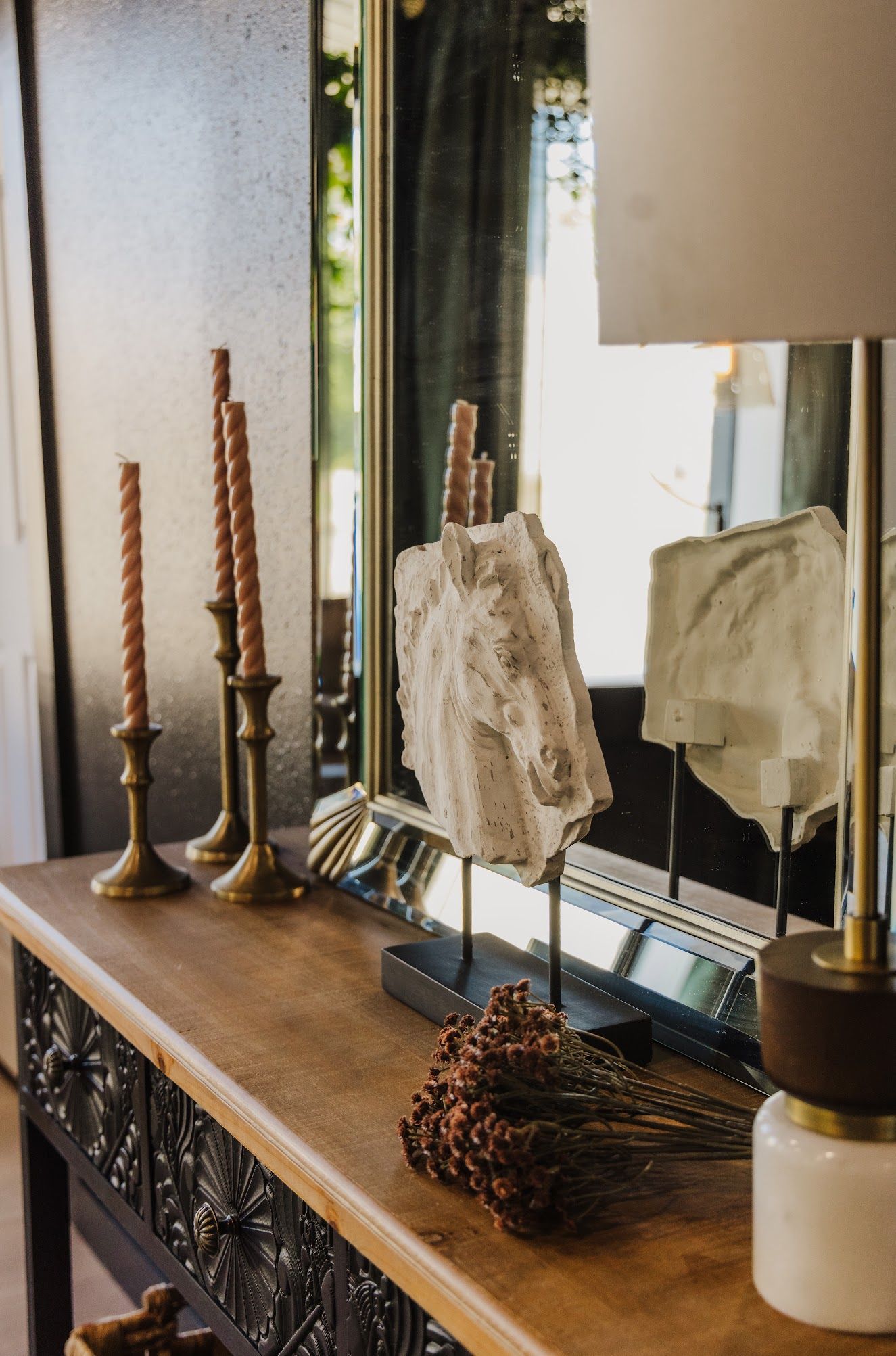 A wooden table with candles , a lamp and a mirror on it.
