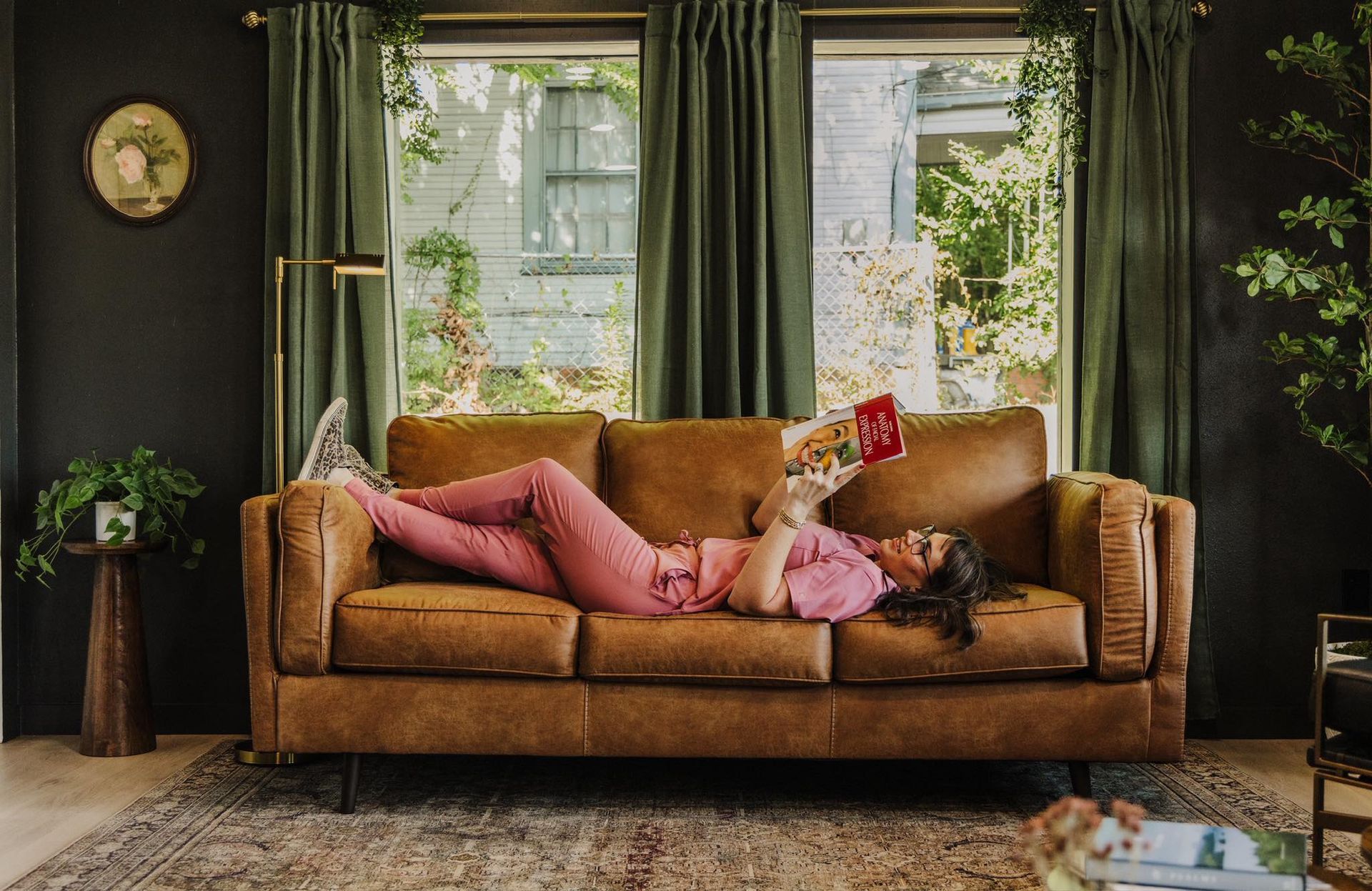A woman is laying on a couch reading a book.