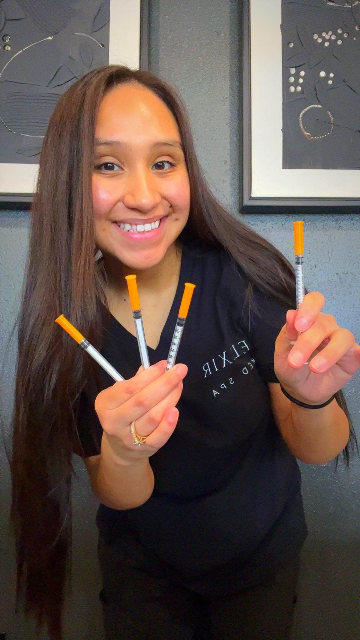 A woman is holding three syringes in her hands and smiling.
