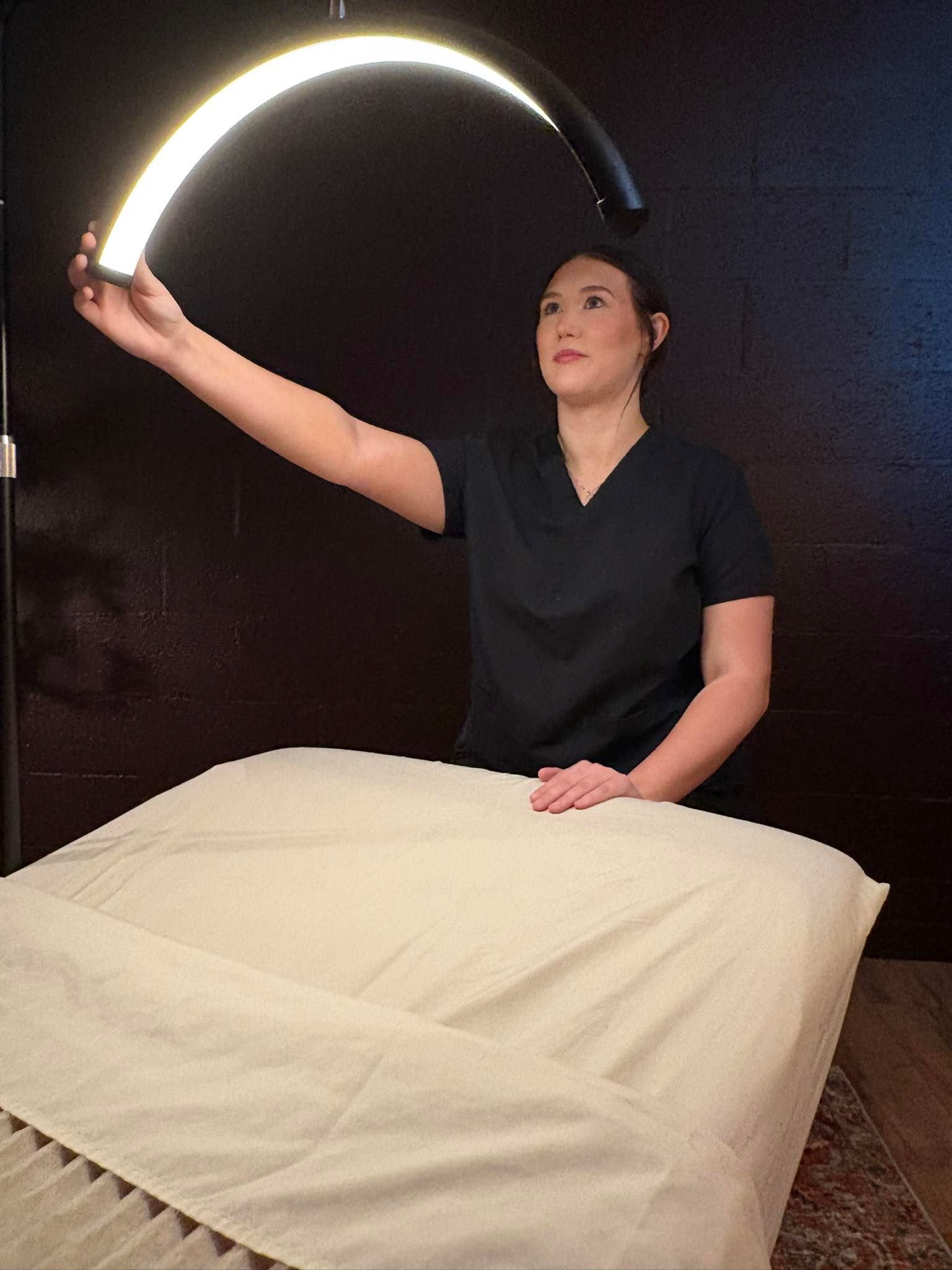 A woman is standing in front of a massage table holding a light.